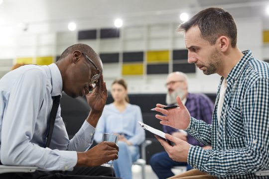 Side view portrait of mature psychologist consulting African man in therapy session, copy space