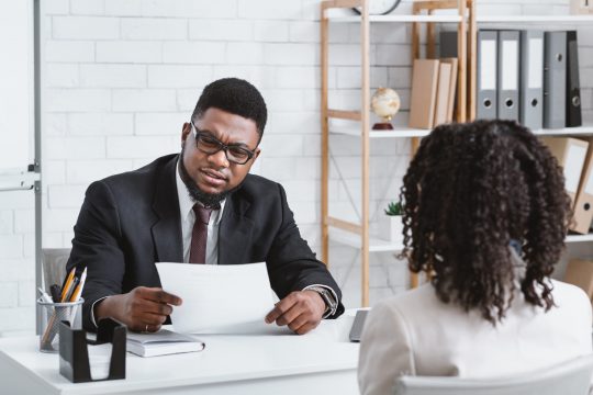 Job search concept. Serious HR manager looking through applicant's resume during employment interview at office